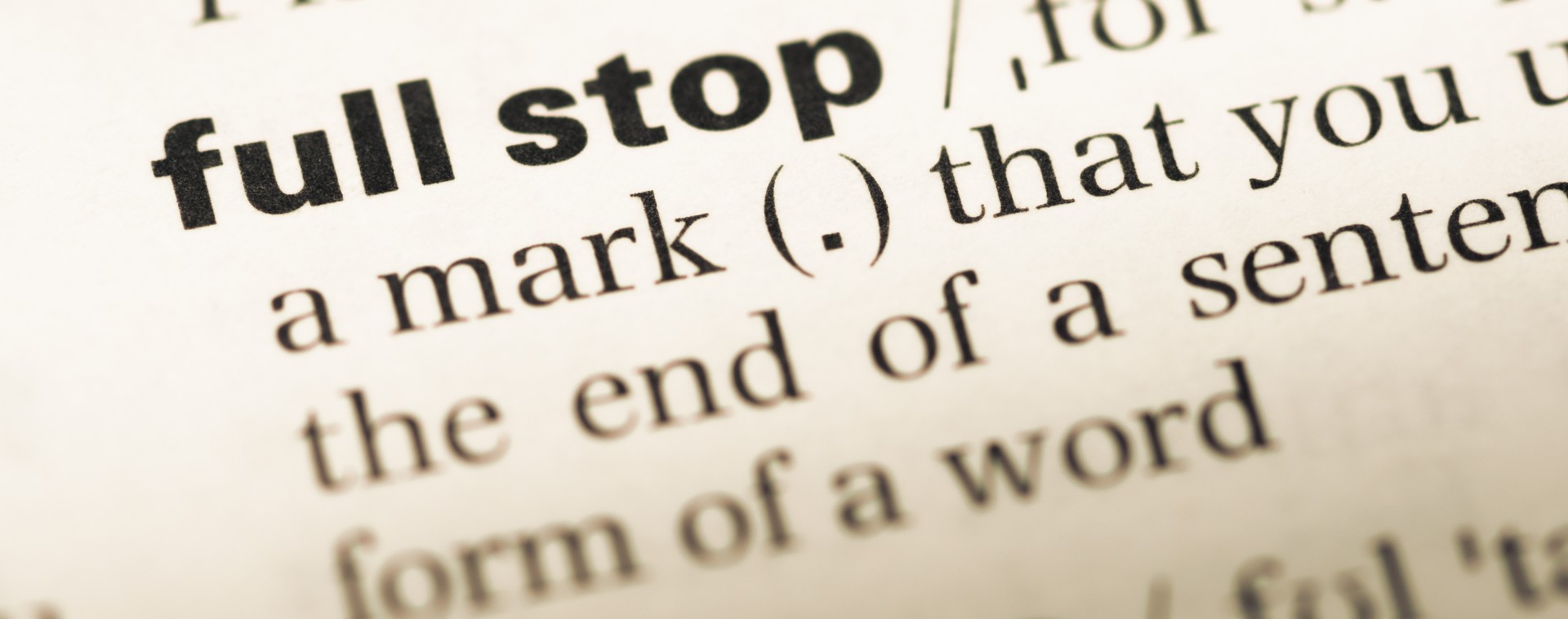 Close-up image of a dictionary page defining the term "full stop" as a punctuation mark used to indicate the end of a sentence.