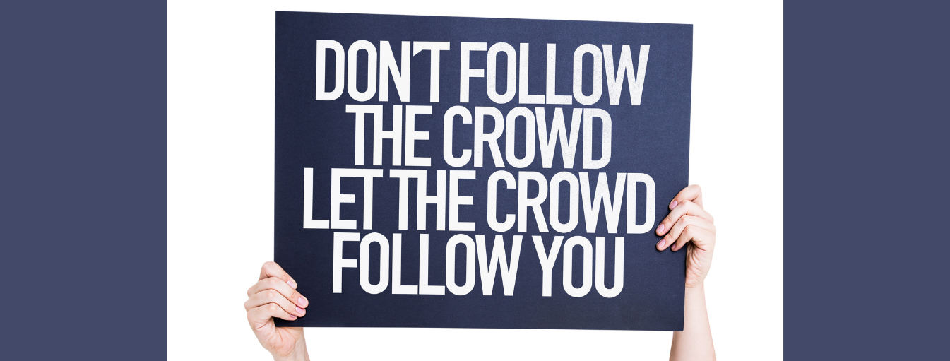 Hands holding a black sign with white text that reads, "DON'T FOLLOW THE CROWD LET THE CROWD FOLLOW YOU.