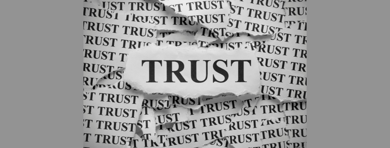 A torn piece of paper with the word "TRUST" visible in the center, surrounded by repeated, smaller versions of the word "TRUST" in the background.