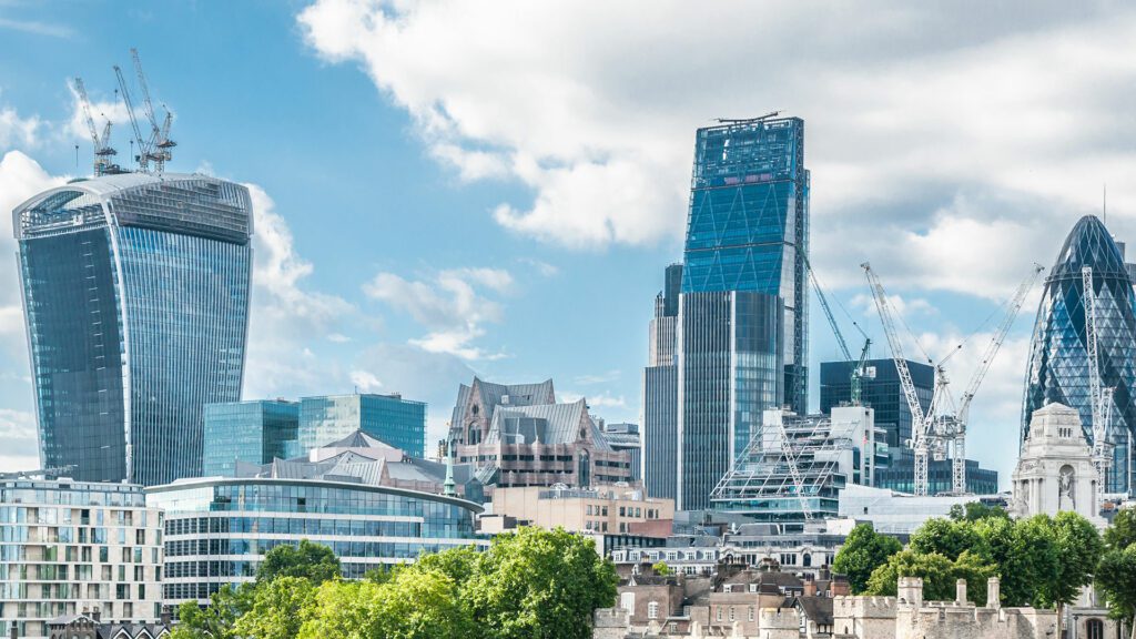 London cityscape featuring modern skyscrapers, including the Walkie Talkie, the Cheesegrater, and the Gherkin, under a partly cloudy sky. Cranes are visible indicating ongoing construction.